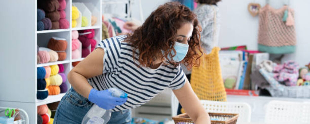 Horizontal view of cleaning lady sanitizing a retail shop while people is buying clothes. Hygienic and preventive measures on pandemic lifestyle.